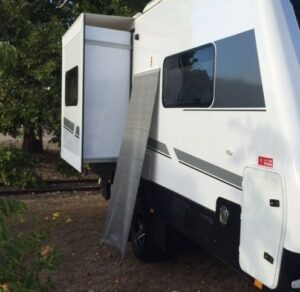 A Caravan RV Fridge Vent Shade Screen with Sail Track 95% shade rating parked next to a tree.