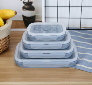Four stackable, rectangular silicone food containers with lids on a kitchen counter.