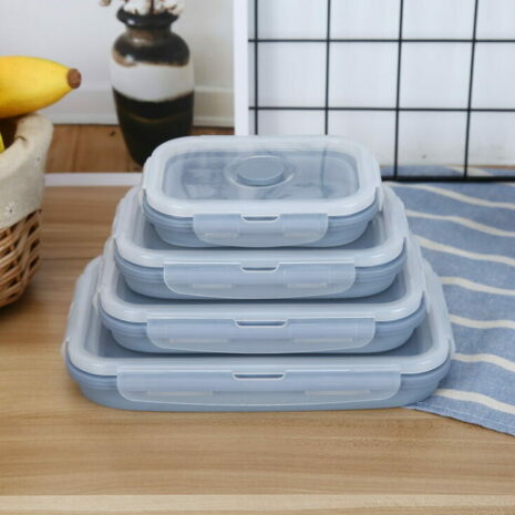Four stackable, rectangular silicone food containers with lids on a kitchen counter.